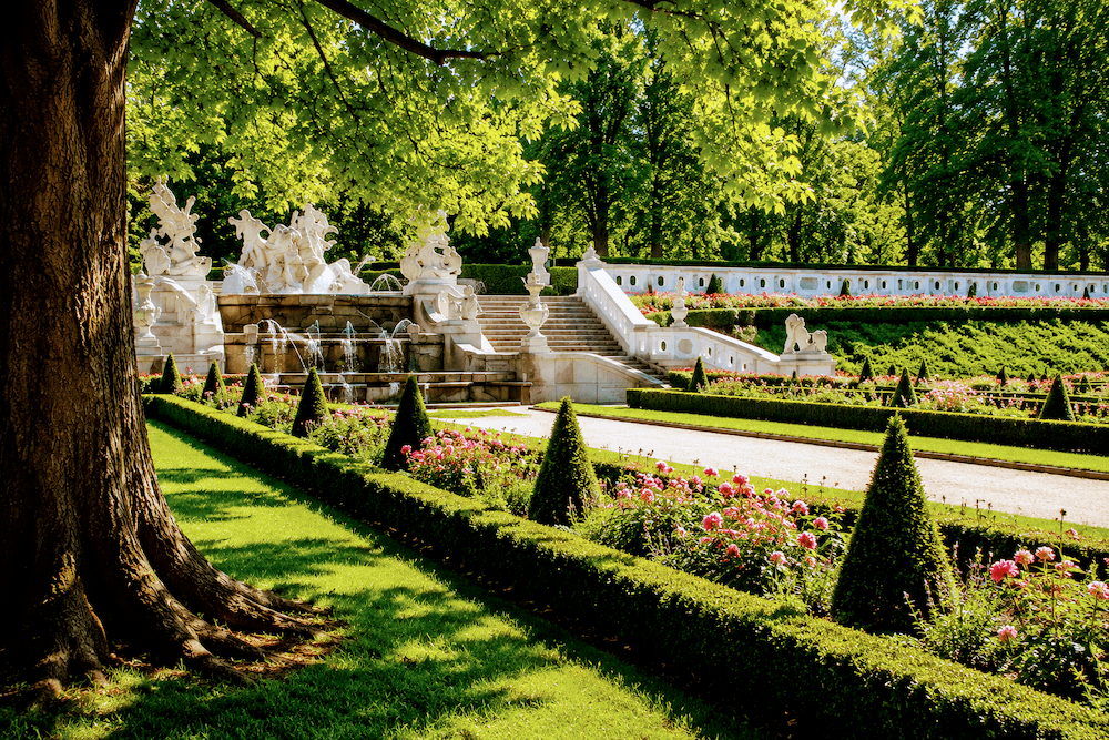 cesky-krumlov-castle-gardens Illustration of formal castle gardens inspired by Český Krumlov, with flower beds, fountains, and tree-lined paths