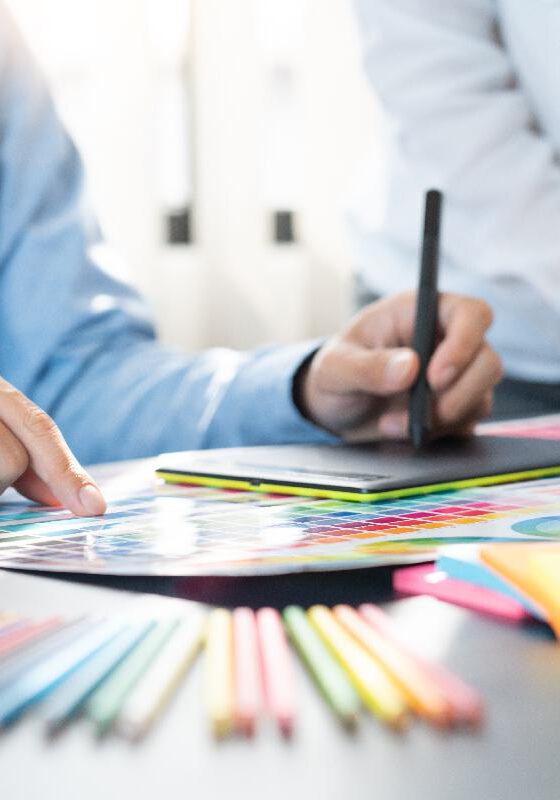 graphic designer team working on web design using color swatches editing artwork using tablet and a stylus at desks In creative office.
